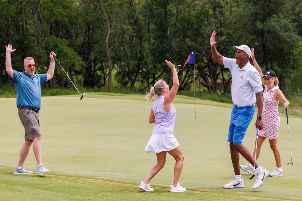 Photo of four people on a golf green, celebrating a good shot with two high-fiving.