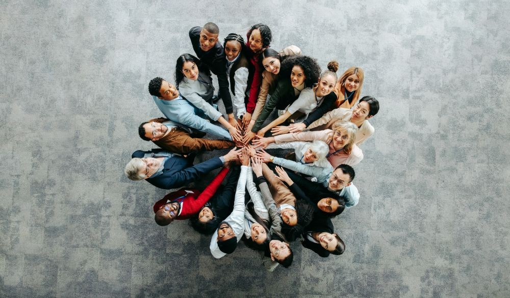 image of a bunch of people standing in a circle, with their extended hands touching in the center.