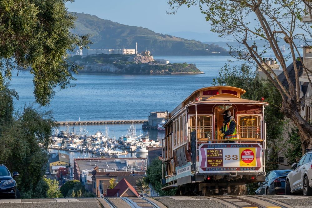 Photo of a cable car climbing a hill in San Francisco, with San Francisco Bay in the distance.