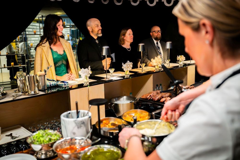 Photo of a chef preparing food in front of a small group of diners at an event.