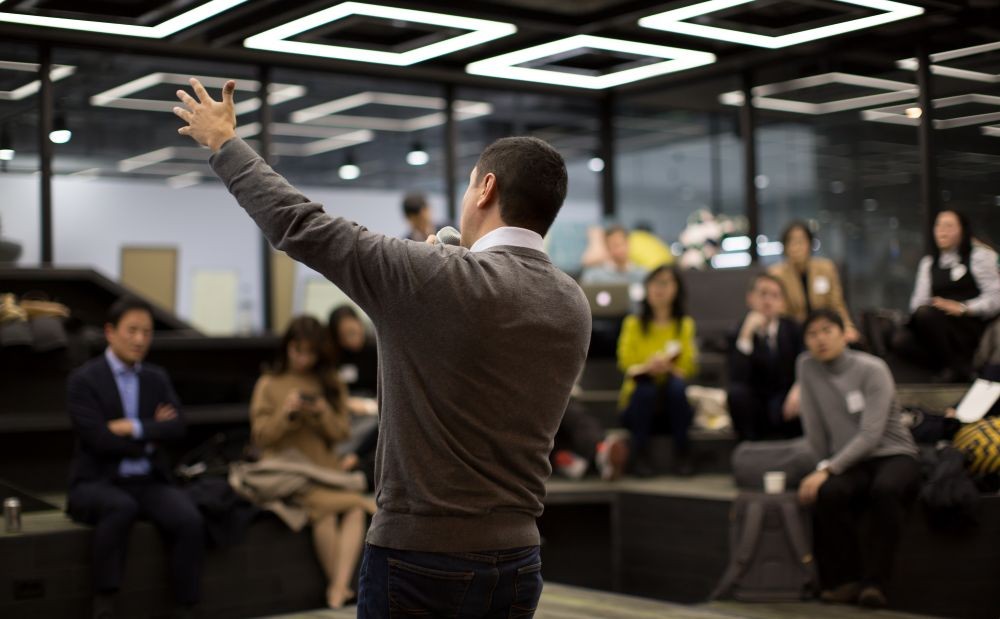 Photo of a man raising his hand while presenting at a meeting.