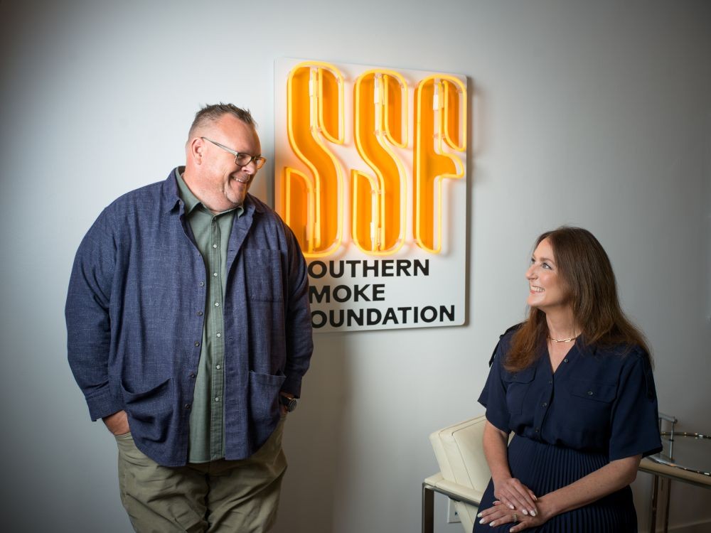 Photo of Chris Shepherd (left, standing) and Lindsay Brown (right sitting) in front of a Southern Smoke Foundation logo.