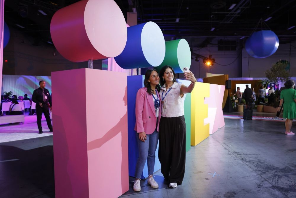 Two attendees take a selfie in front of the IMEX sign