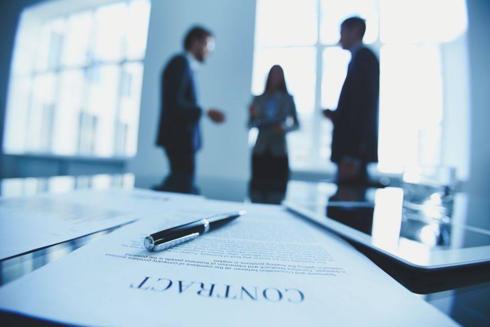 Photo of three people in the background with a contract in the forground.