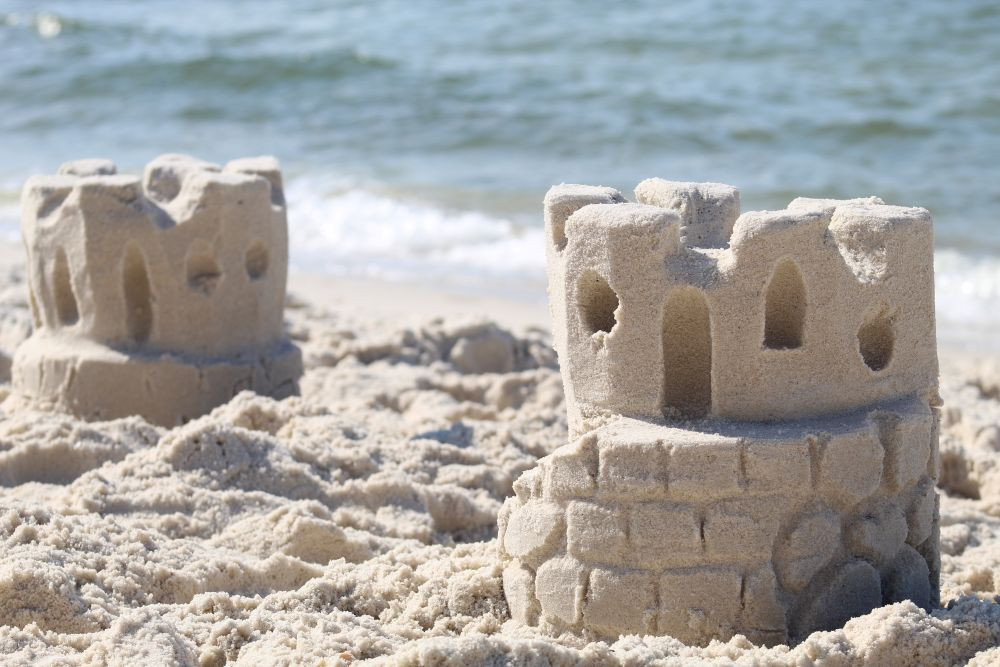 Two sandcastles sit on a sandy beach with the ocean water in the background