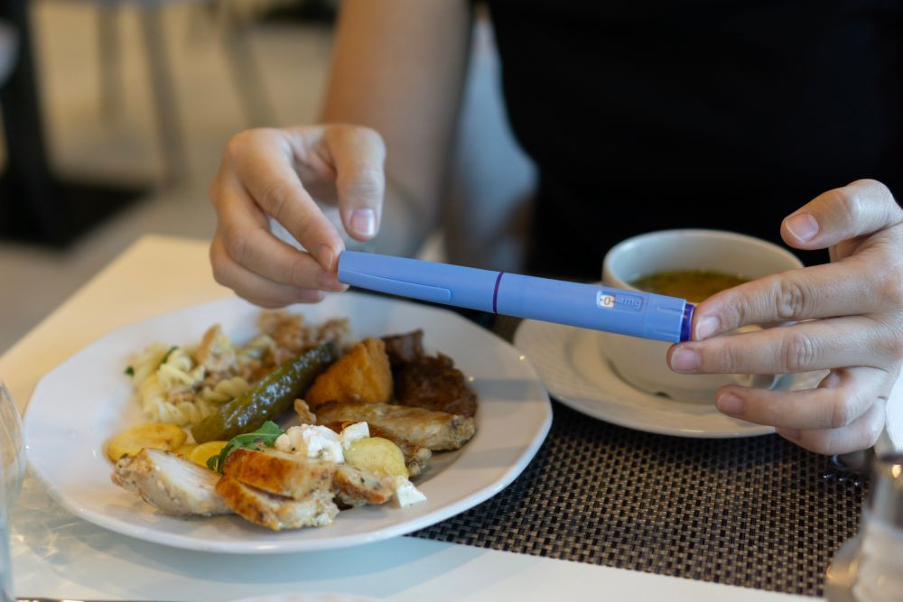 Image of a person with a GLP-1 injection pen next to a plate of food.