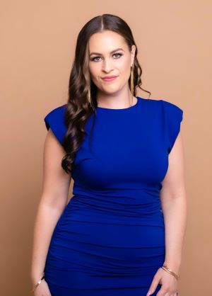 Photo of Courtney Stanley, standing, with a blue dress and a tan background.