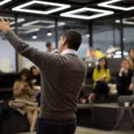 Photo of a man raising his hand while presenting at a meeting.